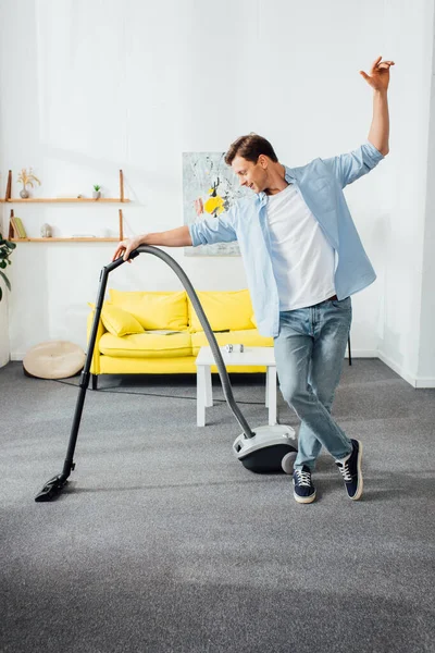 Hombre guapo alfombra de limpieza en la sala de estar con aspiradora - foto de stock