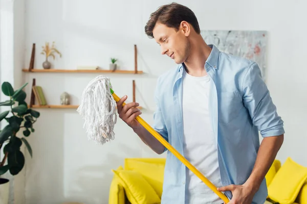 Schöner Mann schaut auf Wischmopp im Wohnzimmer — Stockfoto