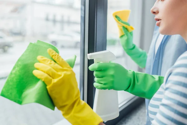 Cropped view of couple with rags and detergent cleaning window at home — Stock Photo