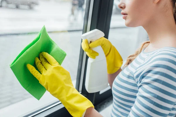 Vista recortada de la mujer usando trapo y detergente mientras limpia la ventana en casa - foto de stock