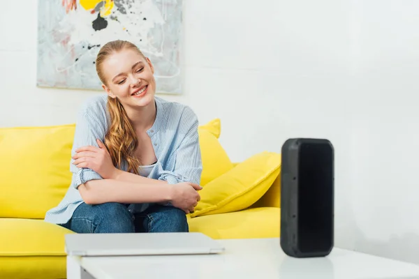 Focus selettivo di donna sorridente vicino altoparlante wireless e laptop sul tavolino in soggiorno — Foto stock