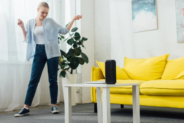 Jolie femme dansant près de haut-parleur portable et ordinateur portable sur la table basse dans le salon — Photo de stock