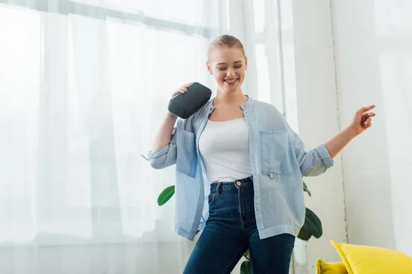 Mujer sonriente bailando mientras sostiene el altavoz inalámbrico en la sala de estar - foto de stock