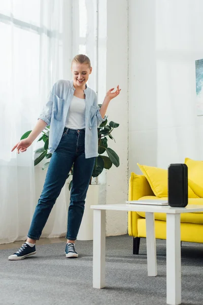 Positives Mädchen tanzt im Wohnzimmer neben tragbarem Lautsprecher und Laptop auf Couchtisch — Stockfoto