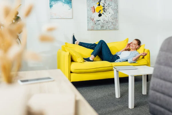 Selective focus of smiling girl in headphones listening music on couch in living room — Stock Photo