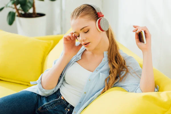 Mulher atraente com olhos fechados ouvindo música em fones de ouvido no sofá — Fotografia de Stock