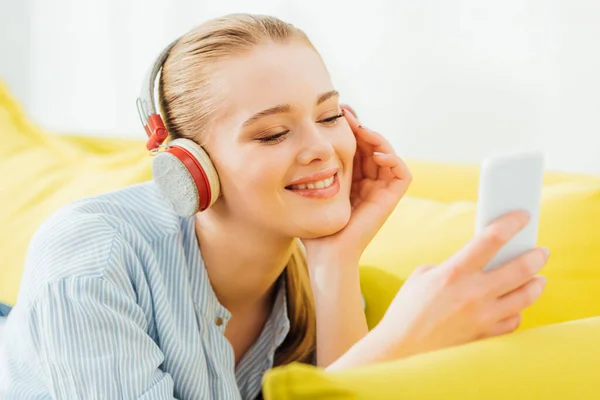 Selective focus of smiling woman in headphones using smartphone on sofa — Stock Photo