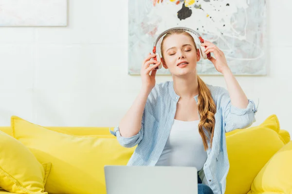 Belle femme écoutant de la musique dans les écouteurs près d'un ordinateur portable à la maison — Photo de stock
