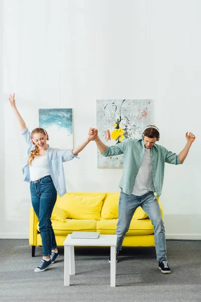 Fröhliches Paar mit Kopfhörern tanzt beim Musikhören im Wohnzimmer — Stockfoto