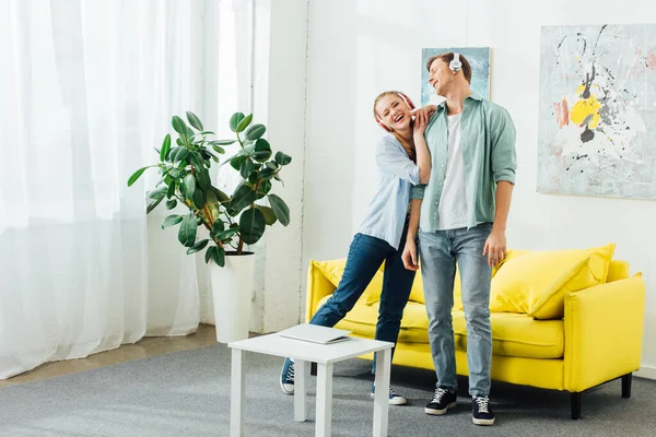 Mujer sonriente en auriculares abrazando novio en la sala de estar - foto de stock