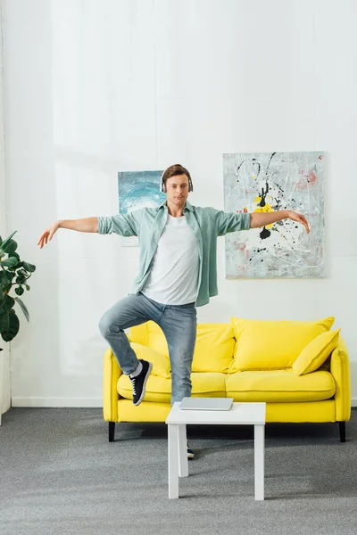 Hombre guapo en auriculares mirando a la cámara mientras baila en casa - foto de stock