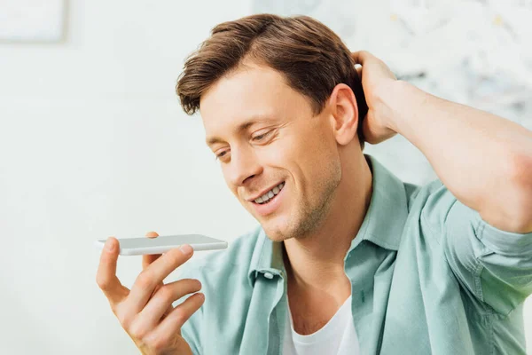 Beau homme souriant tout en utilisant haut-parleur sur smartphone à la maison — Photo de stock