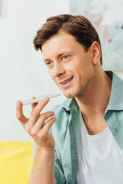 Hombre guapo usando altavoz mientras habla en el teléfono inteligente en casa - foto de stock