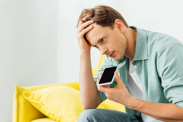 Side view of man using speakerphone while talking on smartphone on yellow couch — Stock Photo