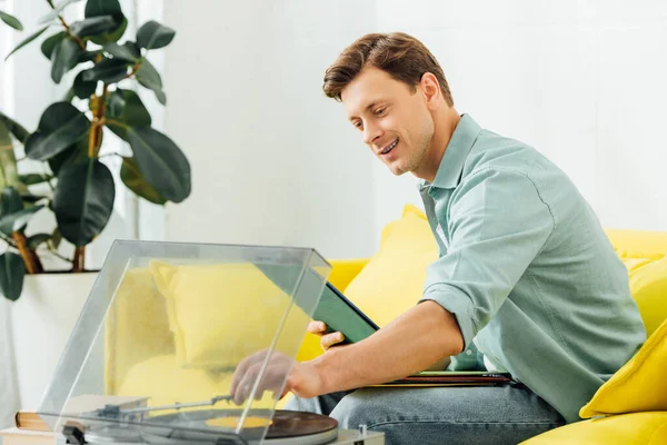 Homme souriant utilisant un tourne-disque sur la table basse dans le salon — Photo de stock