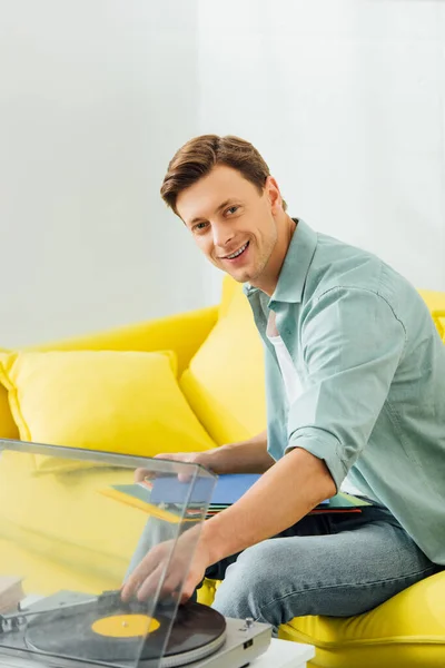 Красивий чоловік, посміхаючись на камеру, тримає вінілові записи біля звукозапису у вітальні — стокове фото