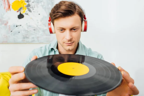 Concentration sélective du bel homme dans les écouteurs détenant un record de vinyle dans le salon — Photo de stock