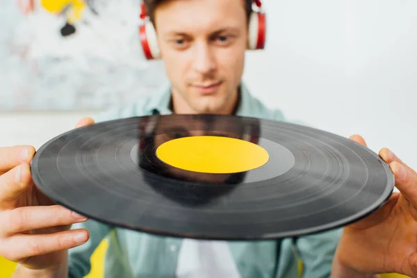 Concentration sélective du jeune homme dans les écouteurs détenant un record de vinyle à la maison — Photo de stock