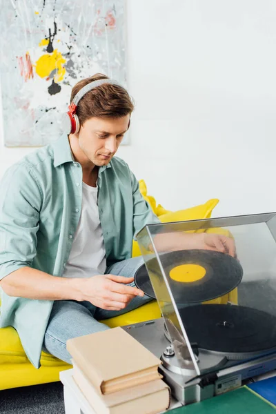 Homme dans les écouteurs en utilisant un tourne-disque près des livres sur la table basse dans le salon — Photo de stock