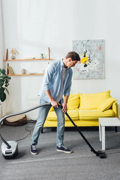 Homme utilisant un aspirateur tout en nettoyant le tapis dans le salon — Photo de stock