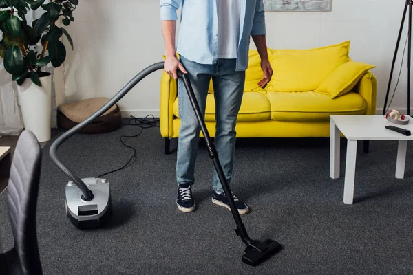 Vista ritagliata dell'uomo che utilizza l'aspirapolvere mentre pulisce il tappeto in soggiorno — Foto stock