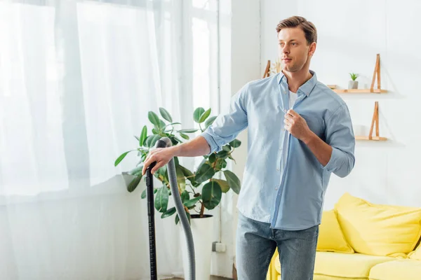 Bell'uomo che distoglie lo sguardo tenendo l'aspirapolvere a casa — Foto stock