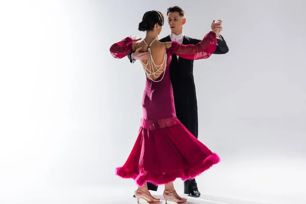 Elegantes junges Tanzpaar in rotem Kleid im Anzug, das auf weißem Grund tanzt — Stockfoto