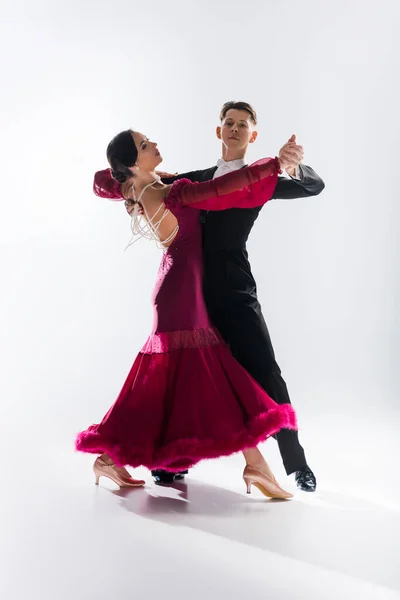 Élégant jeune couple de danseurs de salon en robe rouge en costume dansant sur blanc — Photo de stock
