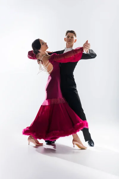 Elegant young couple of ballroom dancers in red dress in suit dancing on white — Stock Photo