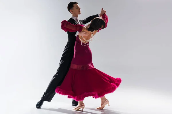 Елегантна молода пара бальних танцюристів в червоній сукні в костюмі танцює на білому — стокове фото