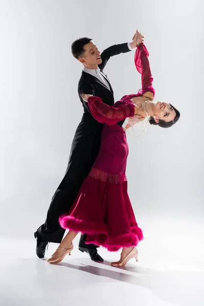 Elegante jovem casal de dançarinos de salão em vestido vermelho em terno dançando no branco — Fotografia de Stock