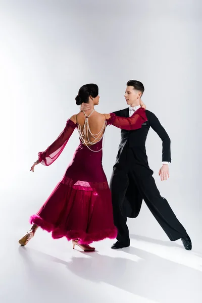 Elegant young couple of ballroom dancers in red dress in suit dancing on white — Stock Photo