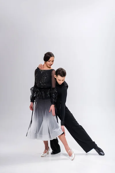 Élégant jeune couple de danseurs de salon en tenue noire dansant sur blanc — Photo de stock