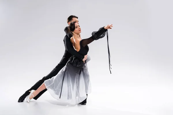Елегантна молода пара бальних танцюристів в чорному вбранні танцює на білому — стокове фото
