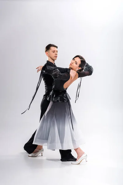 Elegant young couple of ballroom dancers in black outfit dancing on white — Stock Photo