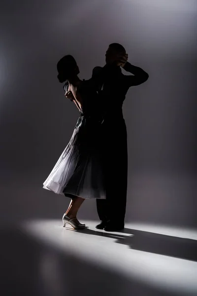 Elegant young couple of ballroom dancers in black outfit dancing in dark — Stock Photo