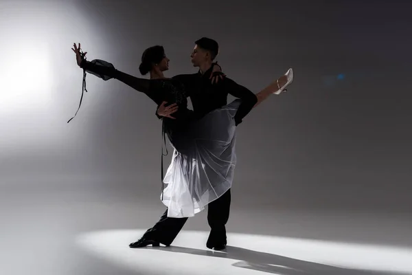 Elegante pareja joven de bailarines de salón en traje negro bailando en la oscuridad - foto de stock