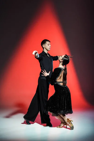 Елегантна молода пара бальних танцюристів танцює в червоному світлі — стокове фото