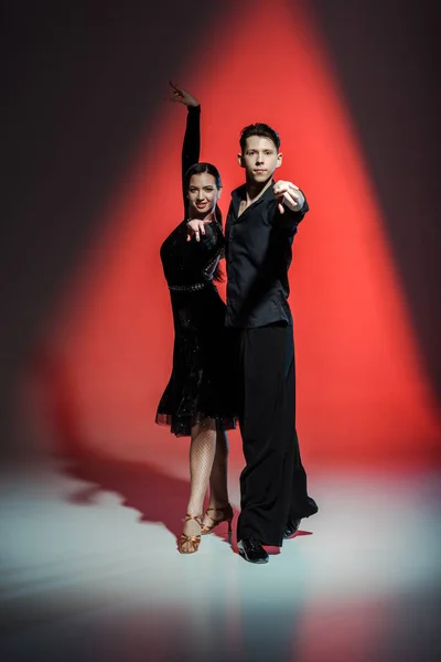 Elegant young couple of ballroom dancers dancing in red light — Stock Photo