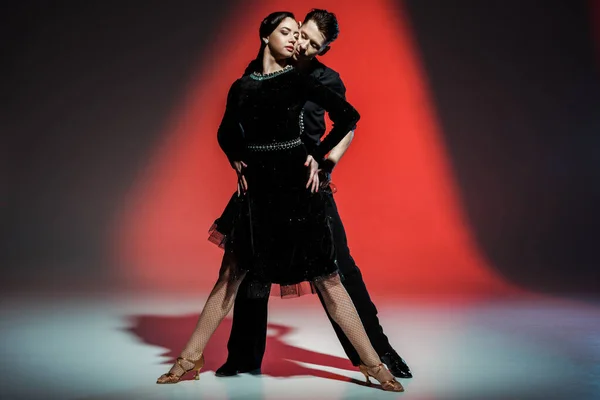 Elegante pareja joven de bailarines de salón bailando en luz roja - foto de stock