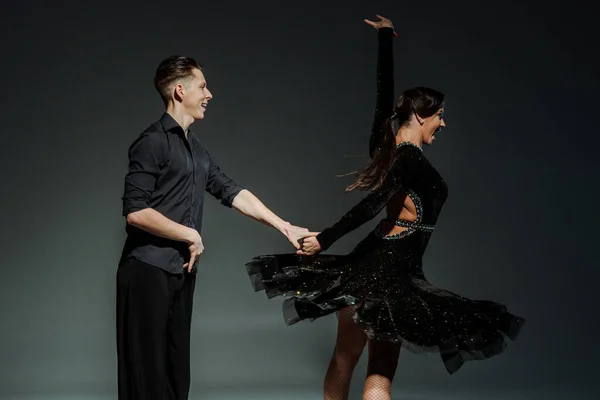 Élégant jeune couple de danseurs de salon en tenues noires dansant dans l'obscurité — Photo de stock