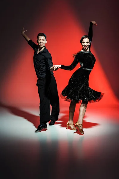 Elegante jovem casal de dançarinos de salão em roupas pretas dançando em luz vermelha — Fotografia de Stock