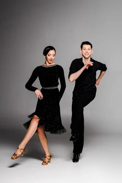 Élégant jeune couple de danseurs de salon en robe noire et costume dansant sur gris — Photo de stock