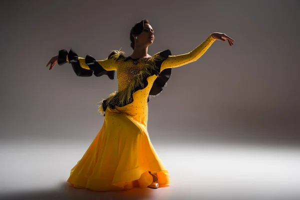 Smiling elegant young ballroom dancer in yellow dress dancing in dark — Stock Photo