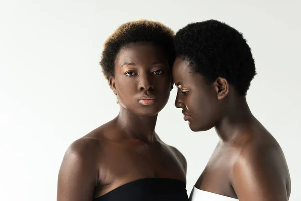 Mujeres afroamericanas en tops tocando frentes aisladas en gris - foto de stock