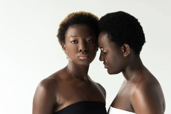 African american women in tops touching foreheads isolated on grey — Stock Photo