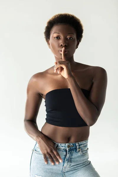 Menina americana africana em jeans e top preto mostrando símbolo de silêncio isolado em cinza — Fotografia de Stock
