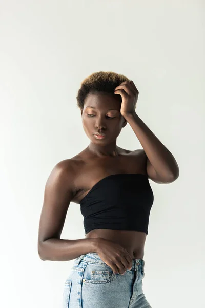 Молодая нежная африканская американка в джинсах и черном топе, изолированная на сером — стоковое фото