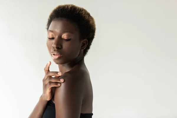 Tenra menina afro-americana em preto top tocando ombro isolado em cinza — Fotografia de Stock