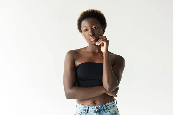 Вдумчивая африканская американка в джинсах и черном топе, изолированная на сером — стоковое фото